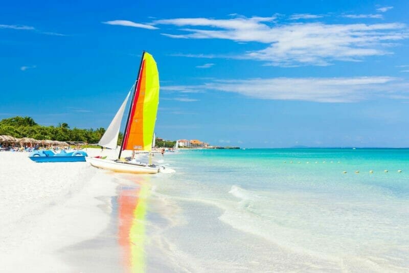 A sunny day ina white sand beach of Varadero in Cuba with a rainbow coloured sailboat