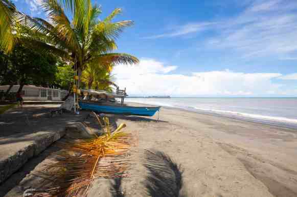 A sandy beach in Panama framed by palm trees. Blue skies and a boat on the sand