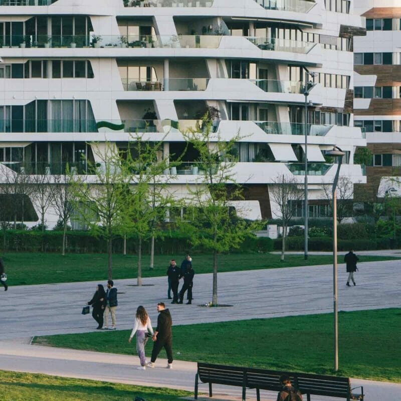 A modern street and a city park with families walking around. 