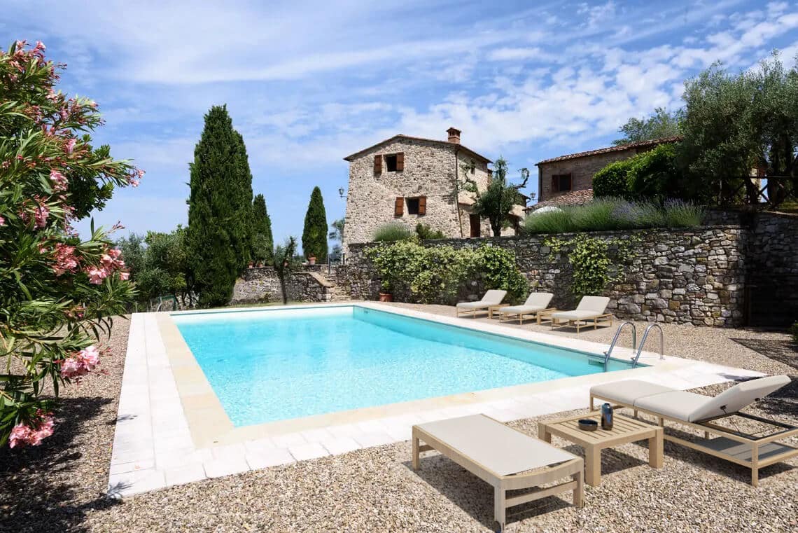 A swimming pool by a beautiful stone country house on a bright sunny day.