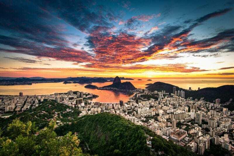 A panoramic view of Rio de Janeiro from a mountain, colorful sunset in the background