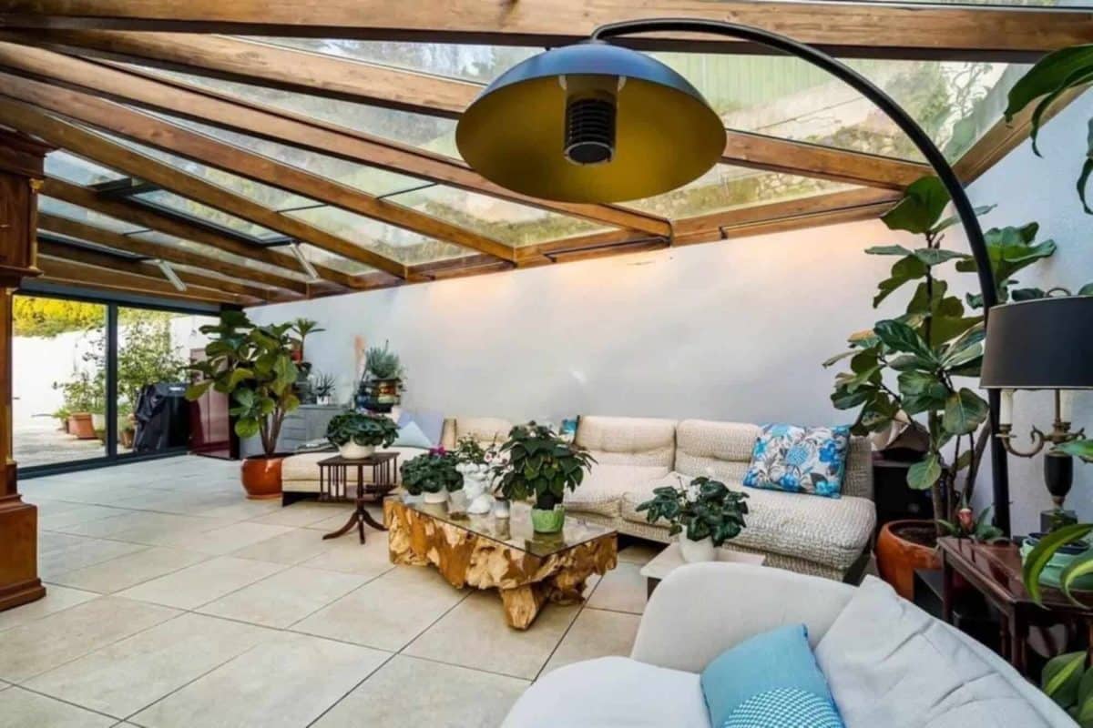 A spacious winter garden room with panoramic windows and glass roof featuring plants and sitting spaces