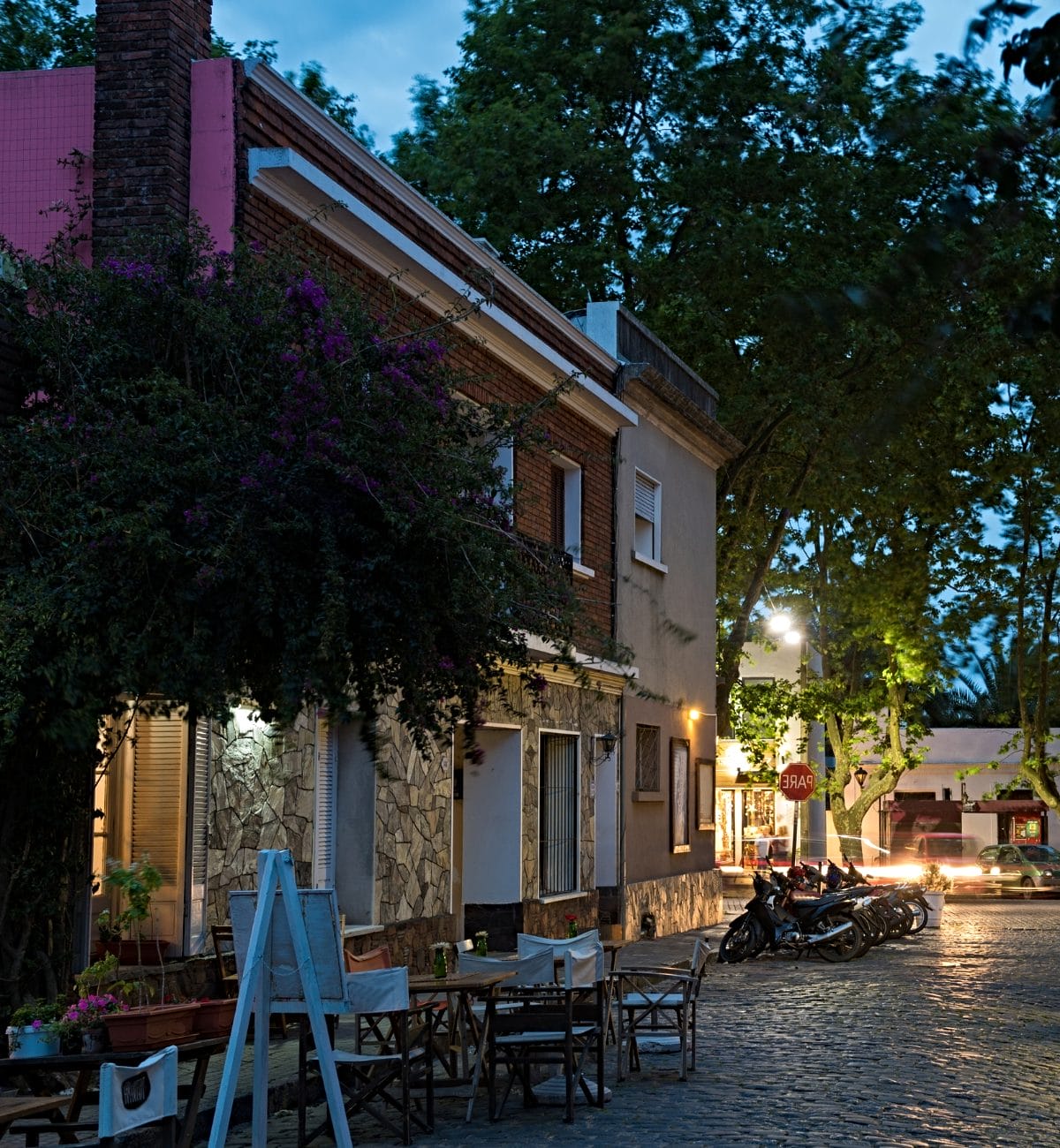 An old narrow paved street of Colonia del Sacramento in the eveningm lit by street lights. a little empty cafe with tables outside, a very cozy atmosphere. 